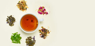 Jasne tło, na którym widnieje filiżanka herbaty a wokół niej różne składniki, z których może być zrobiona